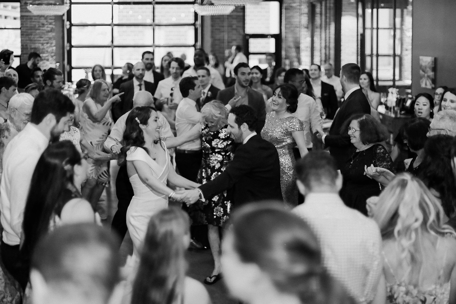 Black-and-white photo of newlyweds dancing among their guests in the brick reception hall