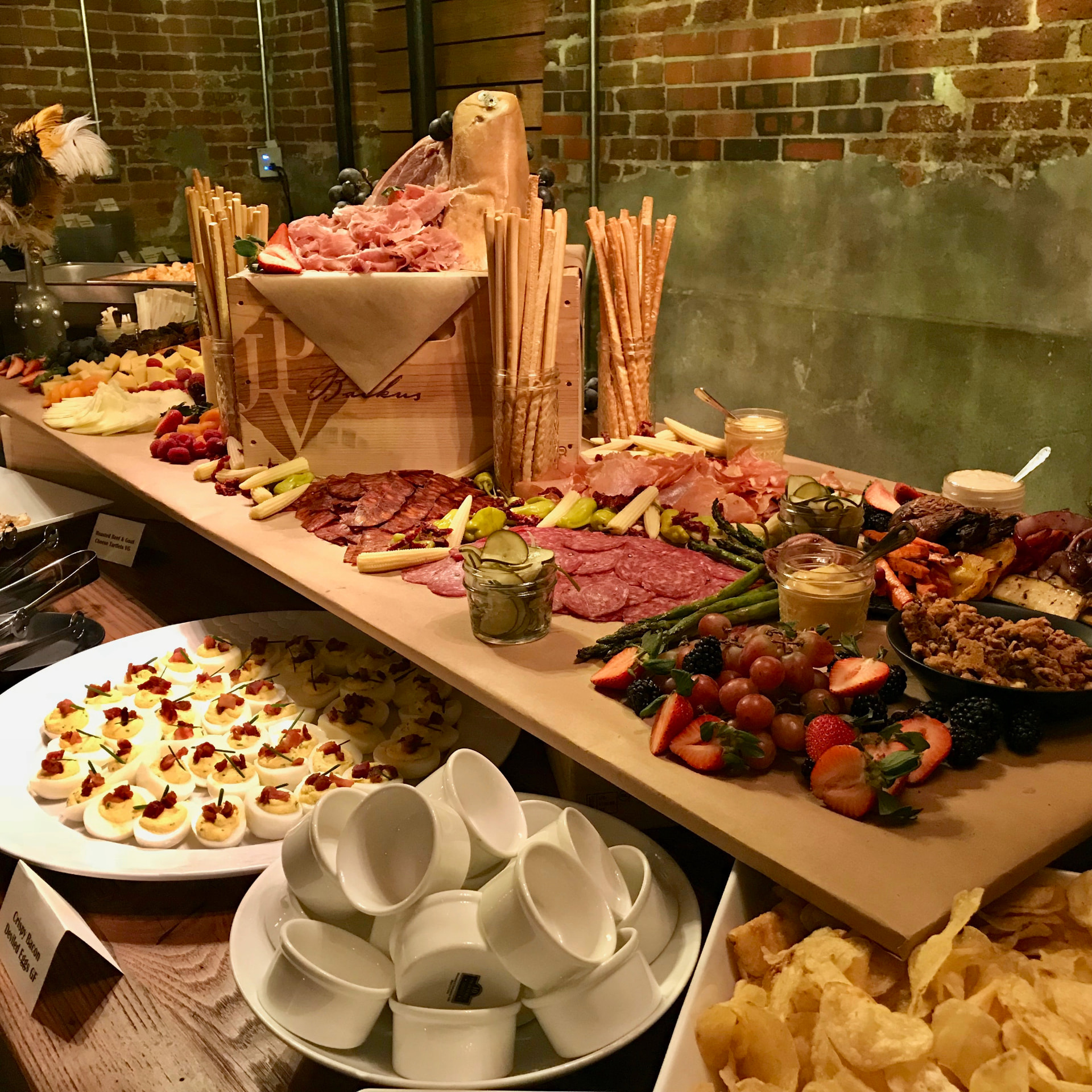 Antipasto display at Bigsby's Folly: a long board of charcuterie, cheeses, grissini, pickles, berries and deviled eggs against exposed brick